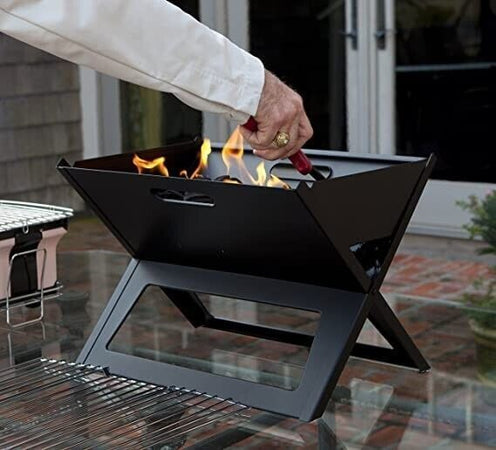 Griglia per barbecue portatile vuota calda con fuoco ardente e carbone di  legna su sfondo nero